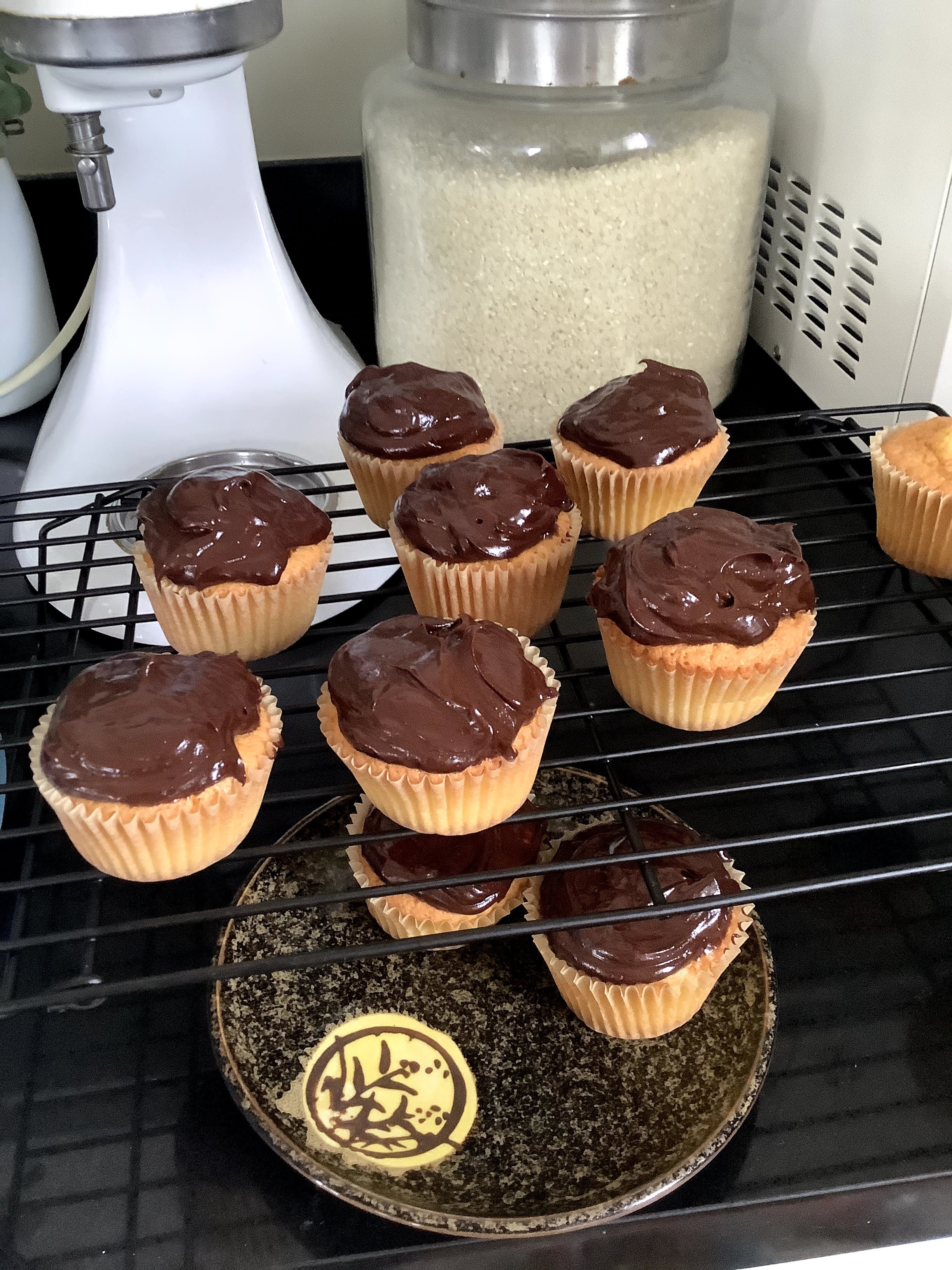 Yellow cupcakes topped with chocolate ganache, on a rack