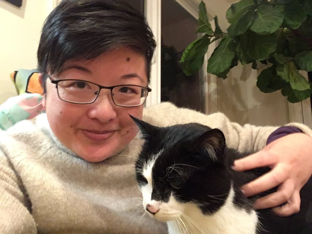 Short-haired Asian person pets a black and white cat on their lap